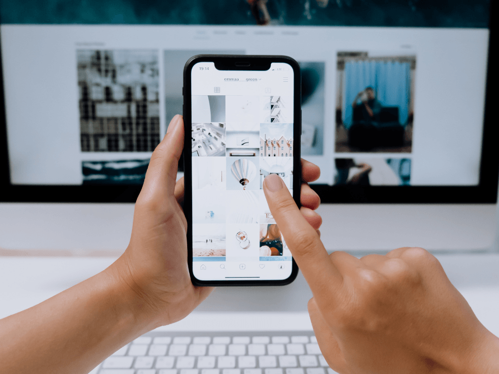 Celular exibindo o feed do Instagram em frente a um computador, representando estratégias para aumentar o alcance orgânico.