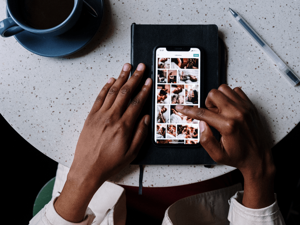 Pessoa navegando pelo feed do Instagram no celular sobre um caderno, em ambiente de trabalho voltado para SEO no Instagram.