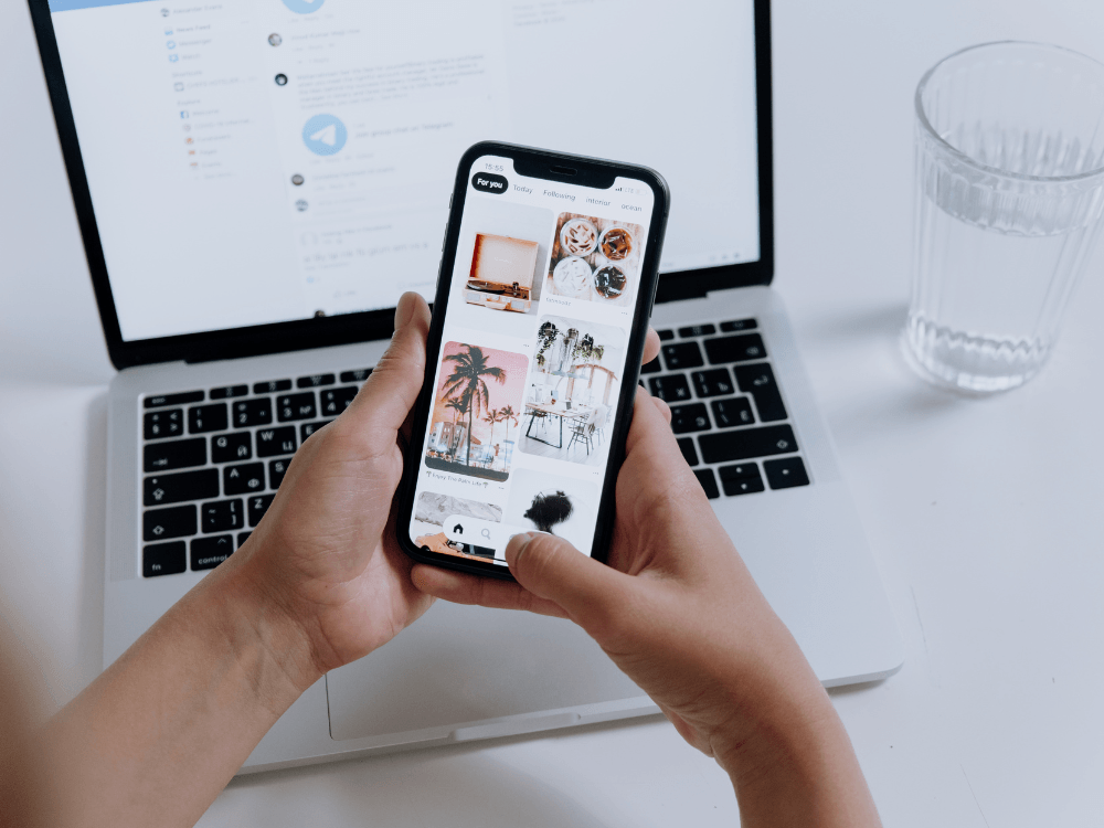 Pessoa utiliza o Instagram no celular enquanto trabalha no notebook, ilustrando estratégias de SEO para ampliar o alcance orgânico.
