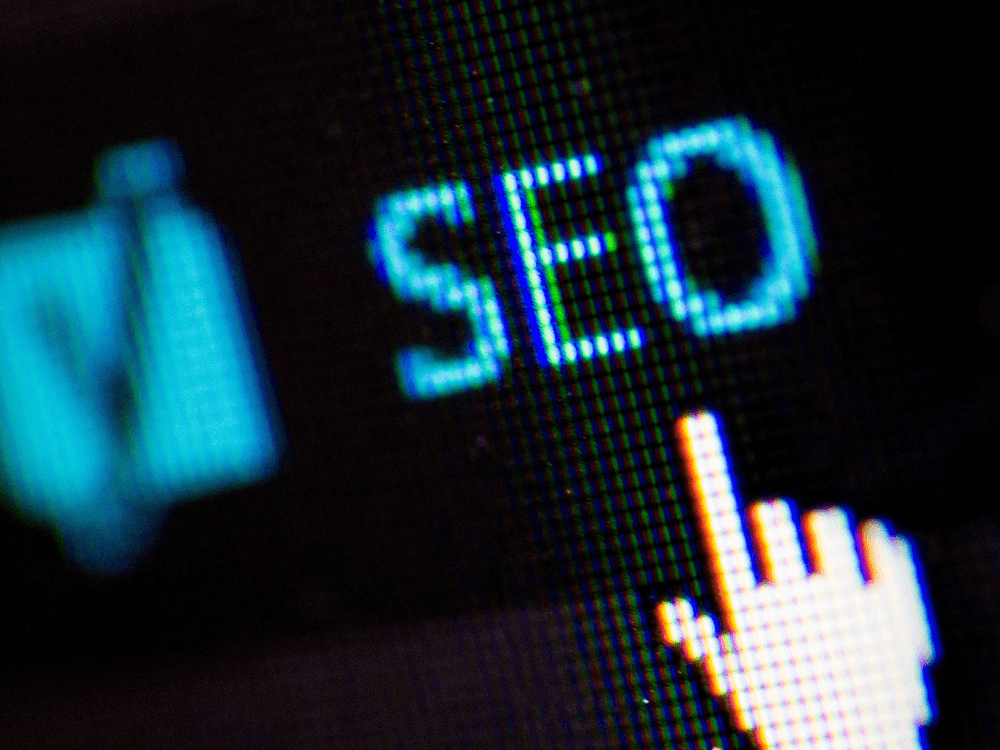 Tela aproximada com a sigla SEO e um cursor, simbolizando ações de otimização para melhorar a presença online de um site.
