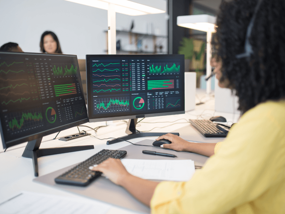 Profissional analisa gráficos e indicadores em dois monitores, representando o acompanhamento do desempenho de um site nas buscas.