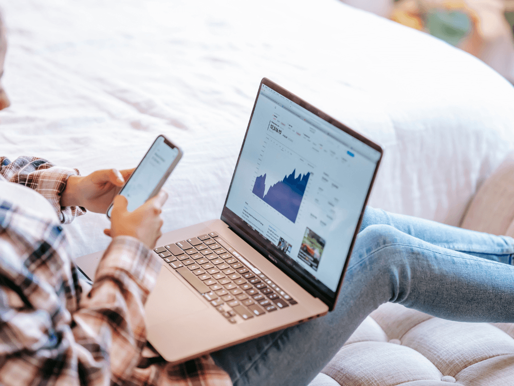 Pessoa utiliza um notebook com gráfico de desempenho e consulta o celular durante uma análise de métricas digitais de um site.