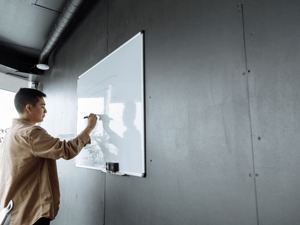 Profissional escreve em um quadro branco durante o planejamento de estratégias, com espaço livre à direita para organizar ideias e informações.