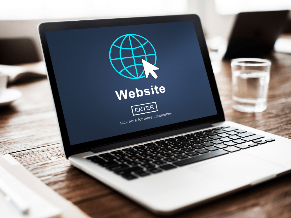 Notebook sobre uma mesa exibe um símbolo de globo com cursor e a palavra Website, representando o acesso a um site na internet.